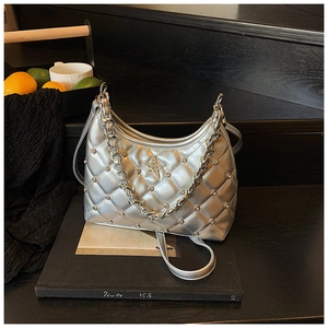 Détail du sac argenté matelassé avec emblème d'étoile et bandoulière chaîne sur socle