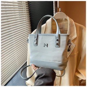 Detailed view of light blue bucket bag with metallic logo and textured synthetic leather finish