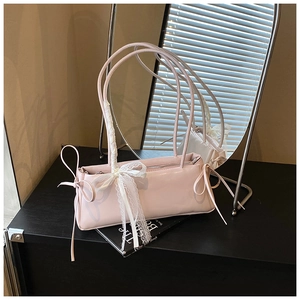 Detail of light pink patent leather handbag featuring a white lace bow on the slim handle