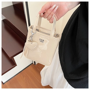 Detail of cream patent leather mini bag with PAN TOR logo and heart-shaped charm