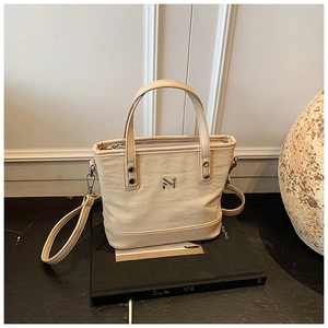 Close-up of beige textured leather bucket bag with metal logo and adjustable shoulder strap