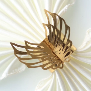 Detailed view of laser-cut gold butterfly paper napkin ring on white fabric