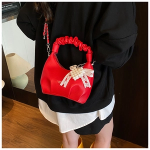 Detail of red ruched handbag featuring pearl heart charm and white lace bow decoration