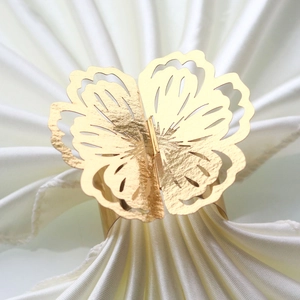 Detailed view of laser-cut gold butterfly napkin ring on white satin fabric