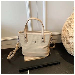 Detail view of beige textured tote bag with metal M logo and detachable strap on decor