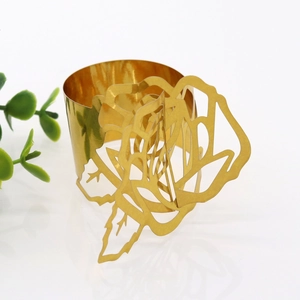 Close-up of a golden metal napkin ring with a hollow rose design on a white background