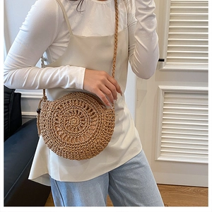 Dettaglio ravvicinato di una borsa a tracolla tonda in paglia con nappe boho e perline in legno