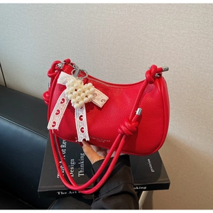 Dettaglio borsa in pelle rossa con fiocco in pizzo bianco e ciondolo a cuore di perla