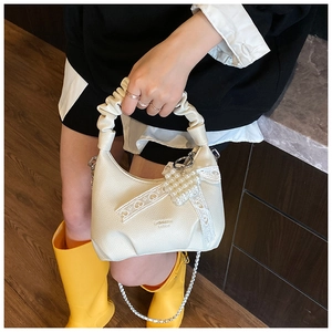 Detailed view of cream leather shoulder bag featuring lace bow and pearl heart pendant