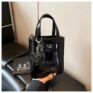 Close-up of black patent leather handbag featuring silver logo and heart charm detail