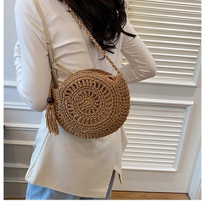 Dettaglio di una borsa a tracolla rotonda in paglia intrecciata con nappe decorative