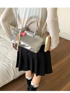 Chic silver metallic bucket bag with heart pendant and woven strap shown on a model