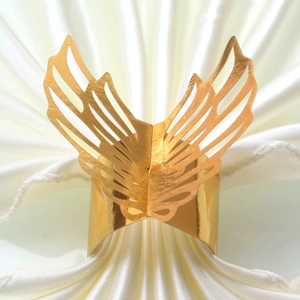 Detailed view of laser-cut butterfly wing napkin ring in glossy gold on white linen
