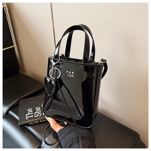 Close-up of black patent leather crossbody bag with heart charm and silver hardware