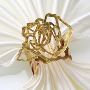 Macro detail of a golden hollow rose napkin ring with shiny metallic glitter texture