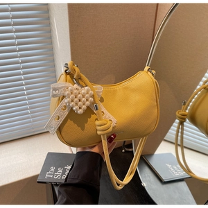 Dettaglio borsa hobo gialla con trama lychee, ciondolo cuore perla e fiocco pizzo