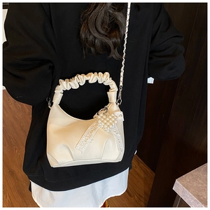Detail of cream leather shoulder bag with chain strap and heart charm on model