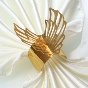 Detailed close-up of golden hollow butterfly napkin ring on a white satin folded napkin