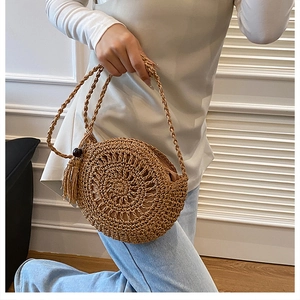 Dettaglio borsa tonda in paglia con texture intrecciata a mano, nappe e perline