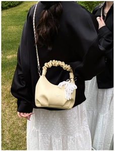 Detail of a creamy yellow lychee leather handbag with cloud handle and pearl lace charm