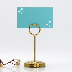 Close-up of a golden metal heart-shaped place card holder with a blue name card on it