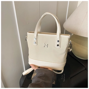 Detail of cream white bucket bag with silver M logo and metallic rivet accents