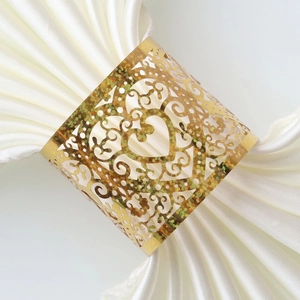 Macro detail of gold glitter heart napkin ring with laser-cut floral patterns on white silk