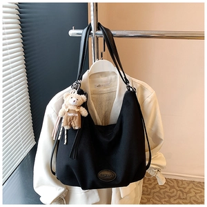 Close-up of black canvas tote bag with a cute plush bear charm and leather logo patch