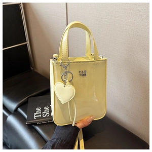Close-up of bright yellow patent leather tote bag with silver logo and heart pendant detail
