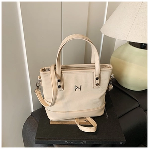 Detailed macro view of the metal M logo and texture on the cream-white bucket bag