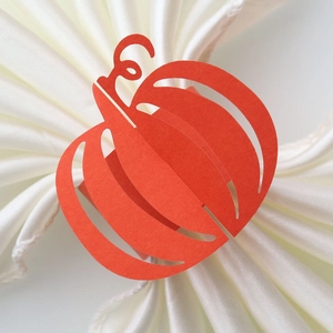 Close-up of orange pumpkin paper napkin ring with laser-cut hollow details on a white cloth