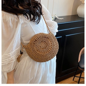 Dettaglio di una borsa a tracolla rotonda in paglia con nappe su un vestito estivo bianco