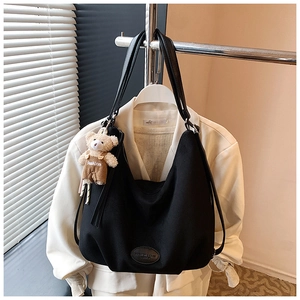 Detail of black large tote bag featuring a cute teddy bear pendant and leather straps