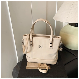 Detailed close-up of cream bucket bag with metal logo and textured synthetic leather