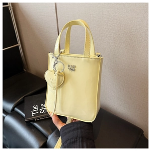 Detail of a light yellow patent leather mini tote with silver PAN TOR logo and heart charm