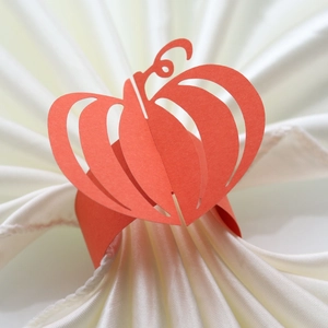 Detailed view of orange paper pumpkin napkin ring on white silk cloth for Halloween