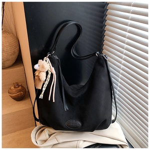 Detail of black hobo tote bag with bear charm and leather tag on a soft fabric base