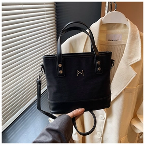 Detail of black faux leather bucket bag with metal logo, top handles and shoulder strap