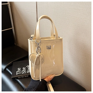 Detail view of glossy cream faux leather handbag with metal logo and heart-shaped charm