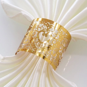 Close-up of golden heart napkin ring with laser-cut vine patterns on a white silk napkin