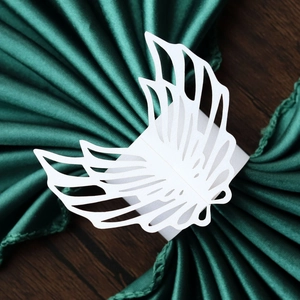 Detail of laser-cut white paper napkin ring in wing design on dark green satin fabric