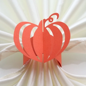 Detailed view of an orange laser-cut paper pumpkin napkin ring for Halloween table decor