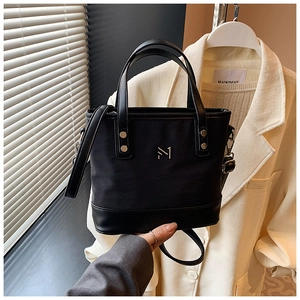 Close-up of black nylon and leather bucket bag featuring a metallic logo and handle details