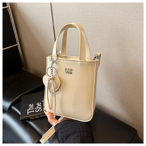 Close-up of cream patent leather handbag featuring a silver logo and heart charm