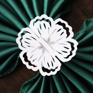 Close-up of white laser-cut floral paper napkin ring on dark green silk fabric