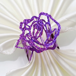 Macro view of purple hollow-out rose napkin ring with shimmering sequins on white fabric