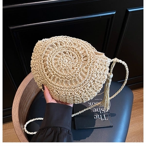 Dettaglio della borsa rotonda in paglia intrecciata beige con nappa e perline in legno