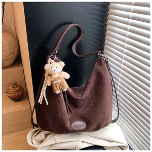 Detail of dark brown faux suede hobo bag with wide shoulder strap and bear charm accessory