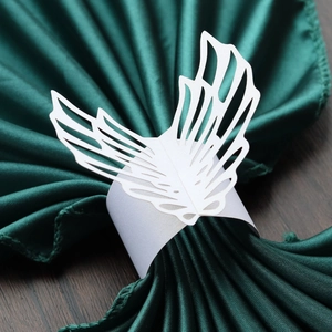 Macro detail of laser-cut white paper angel wing napkin ring on dark green satin fabric