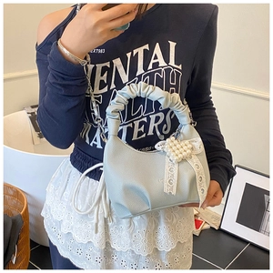 Detail of light blue handbag featuring pearl heart, lace bow and ruched handle
